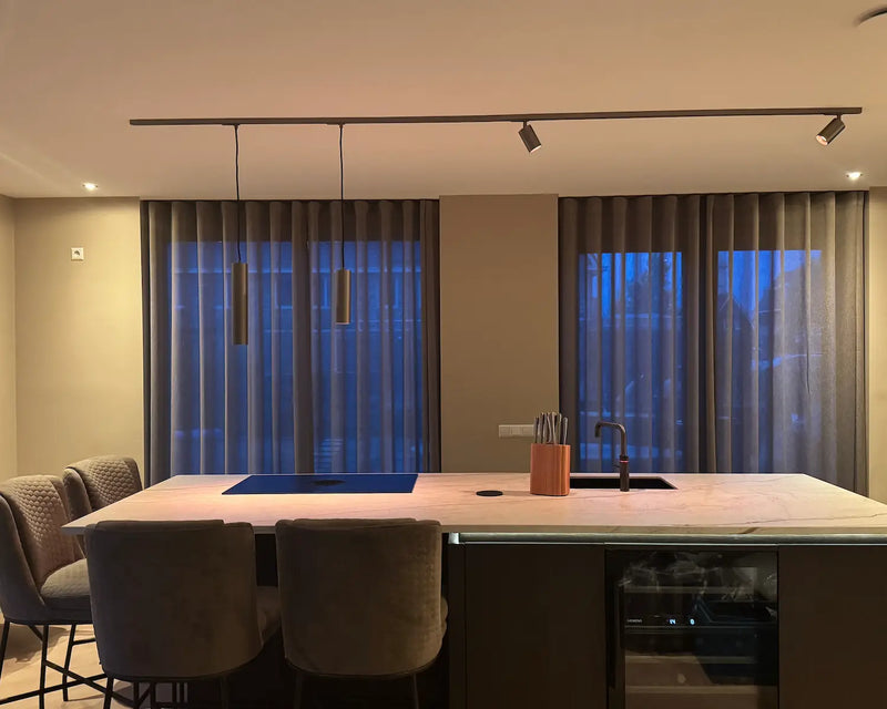 Bronzen railverlichting met twee pendel hanglampen en railspots boven een kookeiland in de avond