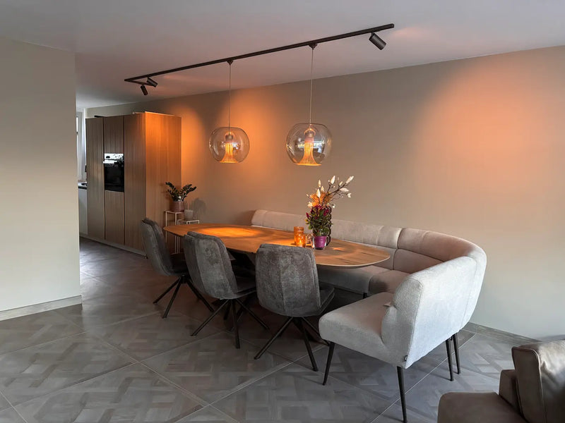 Bronzen railverlichting met richtbare spots en twee glazen lunara hanglampen boven een ovale eettafel